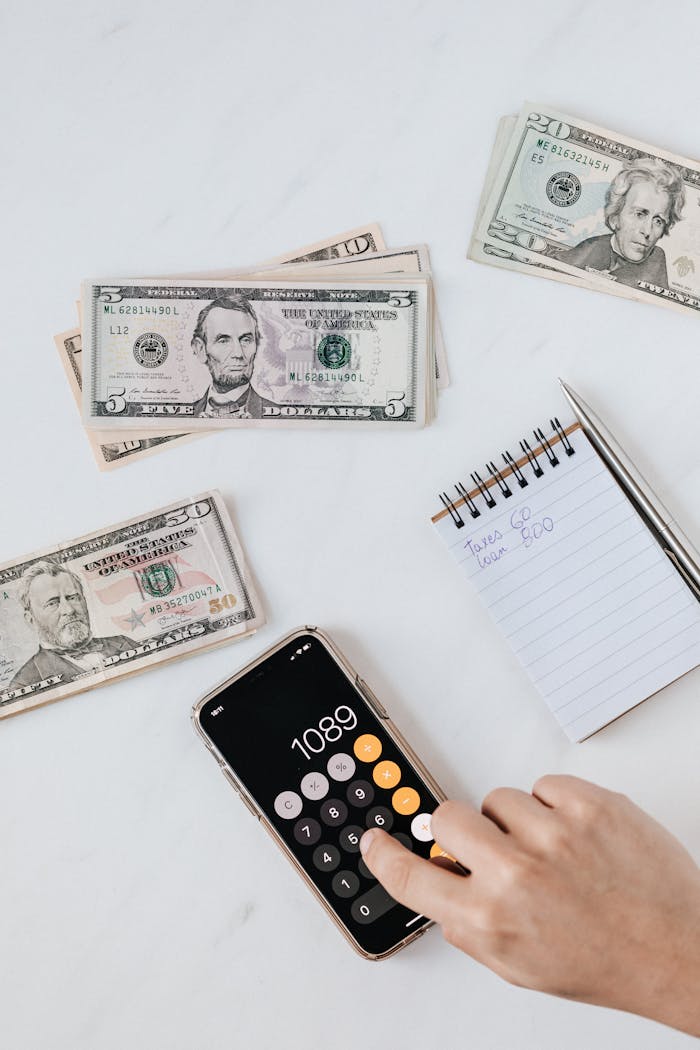 The Art of Drawing Readers In: Your attractive post title goes here From above of crop unrecognizable person using calculator app on cellphone while calculating total amount of money sitting at table with different piles of American dollars and notebook with notes
