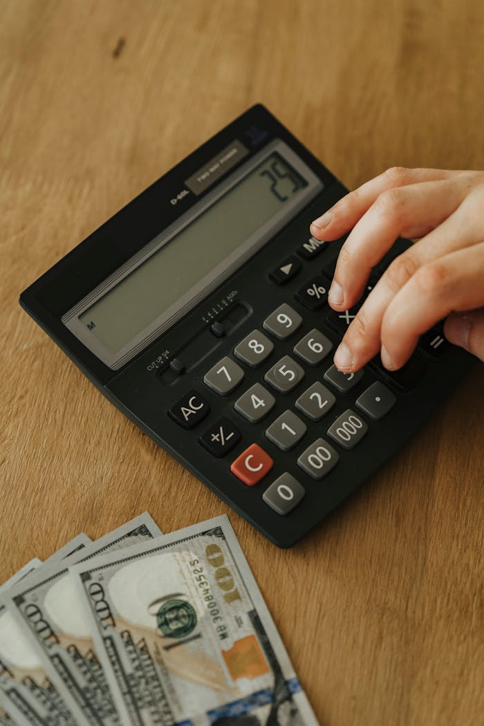 services-02 Hand using a calculator and counting hundred dollar bills on a wooden table, concept of personal finance management.