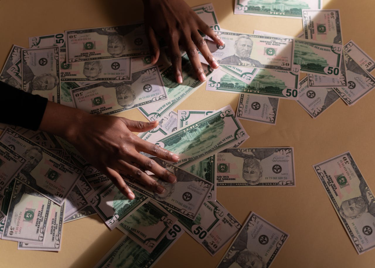 journey-02 Hands arranging multiple US dollar bills on a table, depicting financial abundance and wealth.