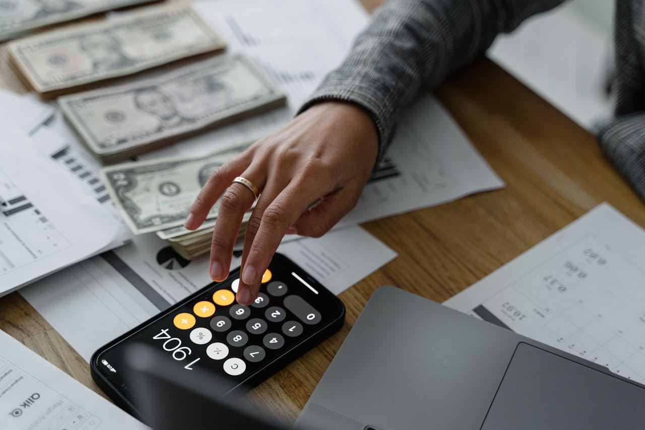 Crafting Captivating Headlines: Your awesome post title goes here Close-up of a person using a smartphone calculator amid money and financial documents on a wooden table.