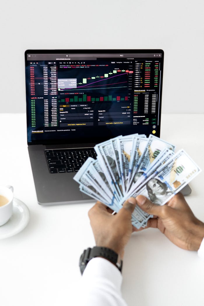 Mastering the First Impression: Your intriguing post title goes here Hands holding cash in front of a laptop displaying stock market data, symbolizing financial growth and investment.