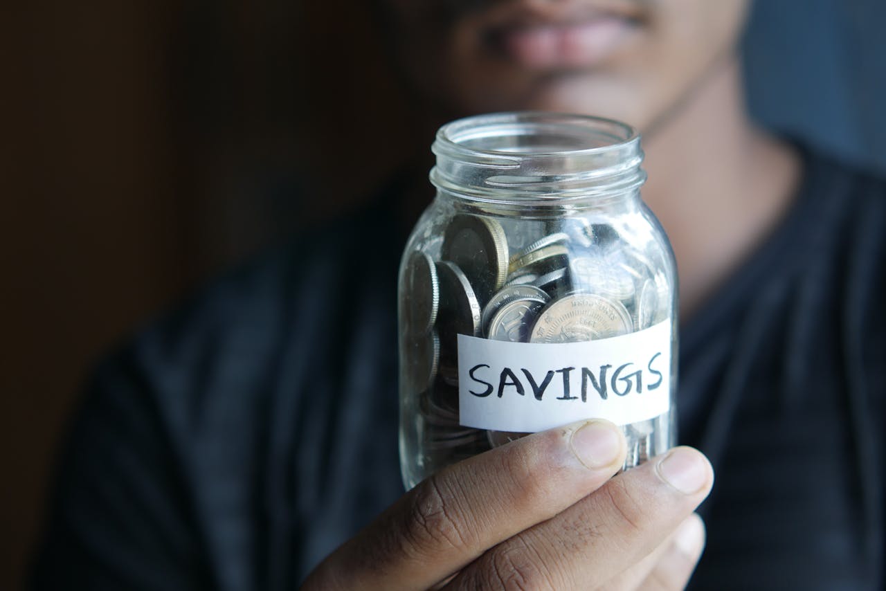 journey-01 A close-up image of a person's hand holding a jar full of coins labeled 'Savings'.